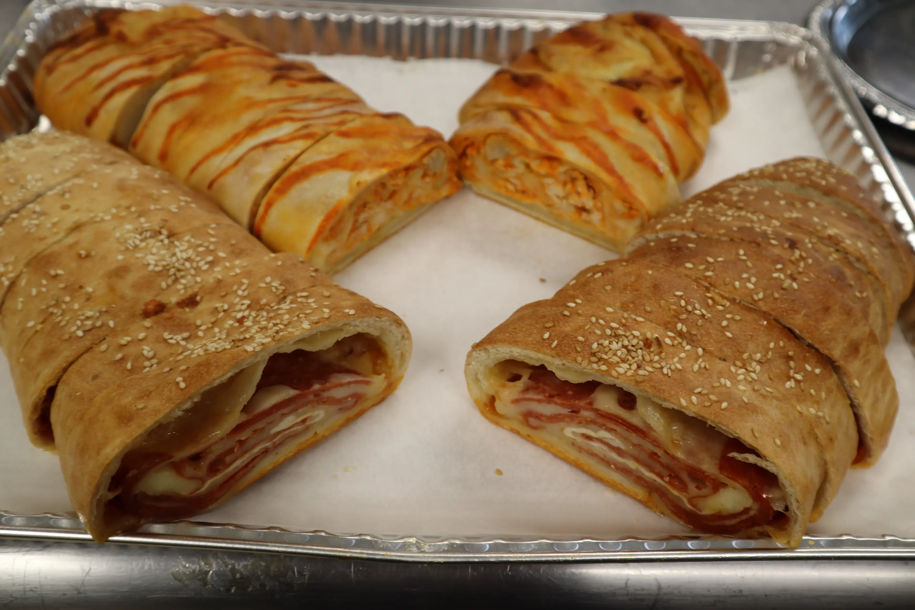 Stuffed breads sliced open to show pepperoni and cheese, on a foil tray