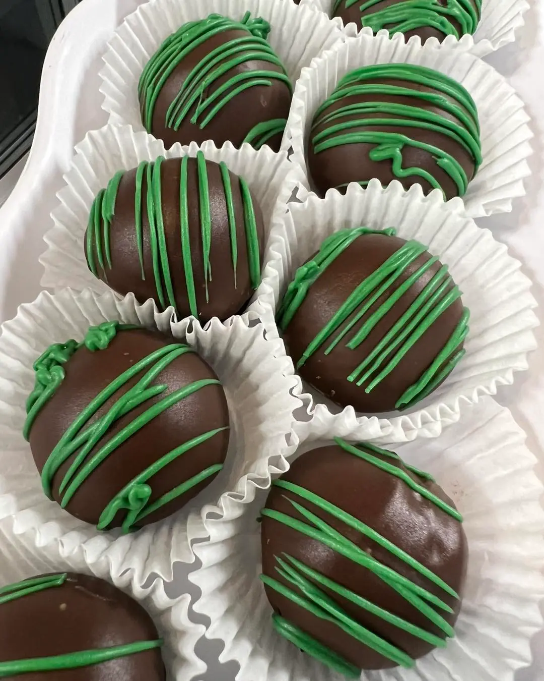 Chocolate-dipped treats with green drizzle in white paper cups