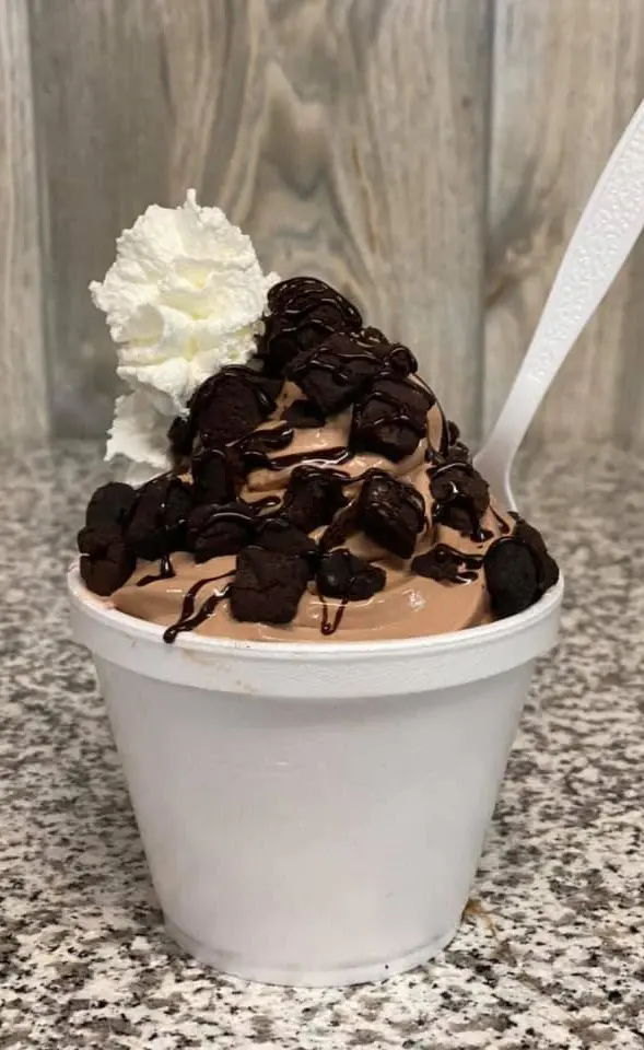 Chocolate soft-serve sundae with brownie pieces, fudge drizzle and whipped cream in a cup